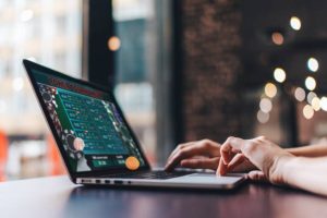 Foto em close-up recortada das mãos de uma garota usando seu laptop para participar de um torneio de pôquer on-line.